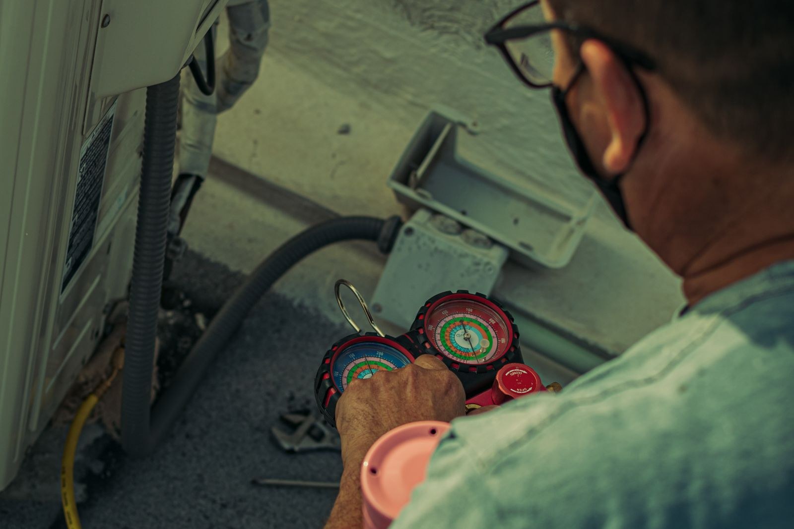 HVAC technician reading refrigerant manifold gauges while servicing an outdoor air conditioning unit